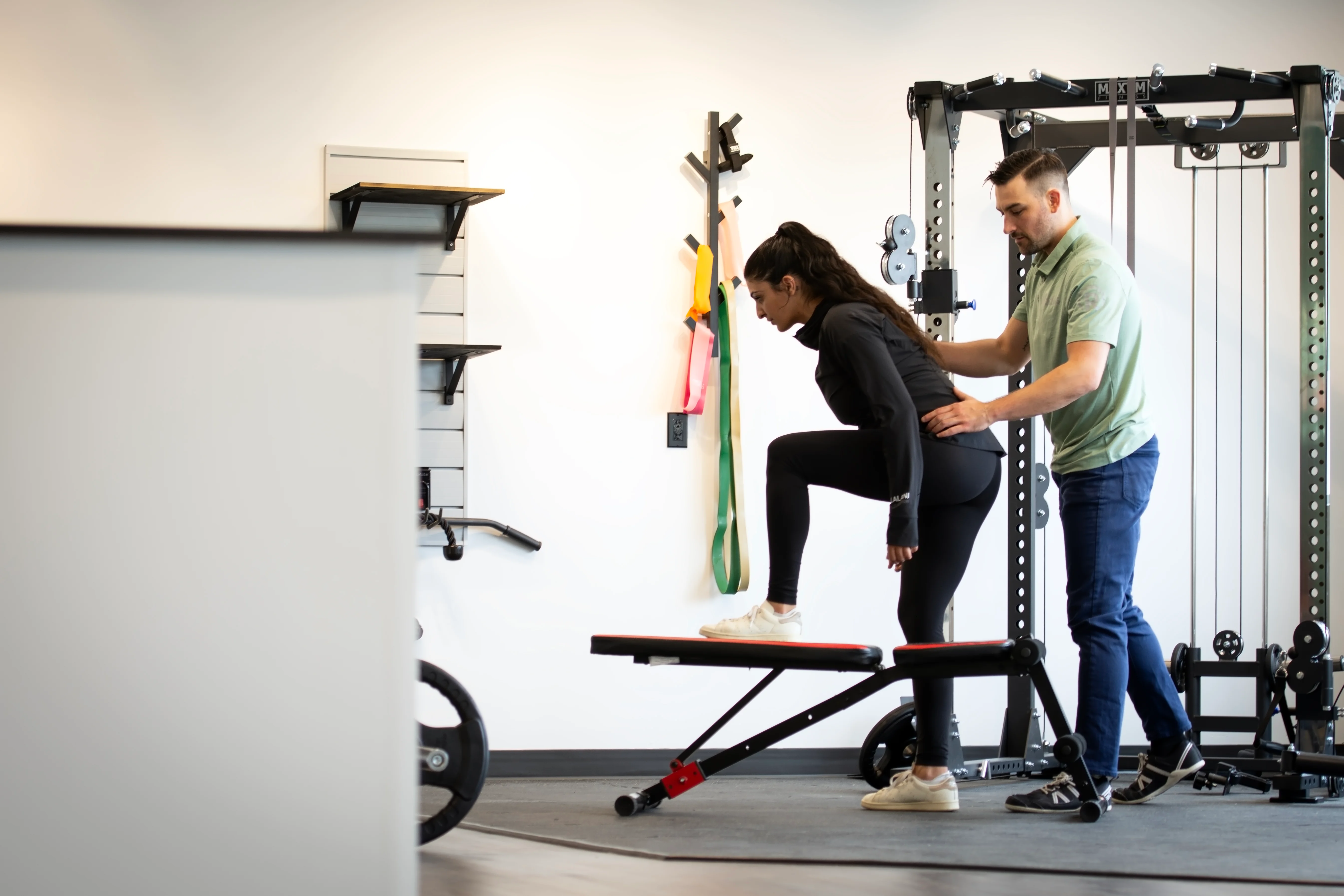 A Radius physiotherapist supporting a patient's hip as she steps up onto a low bench in the clinic gym.