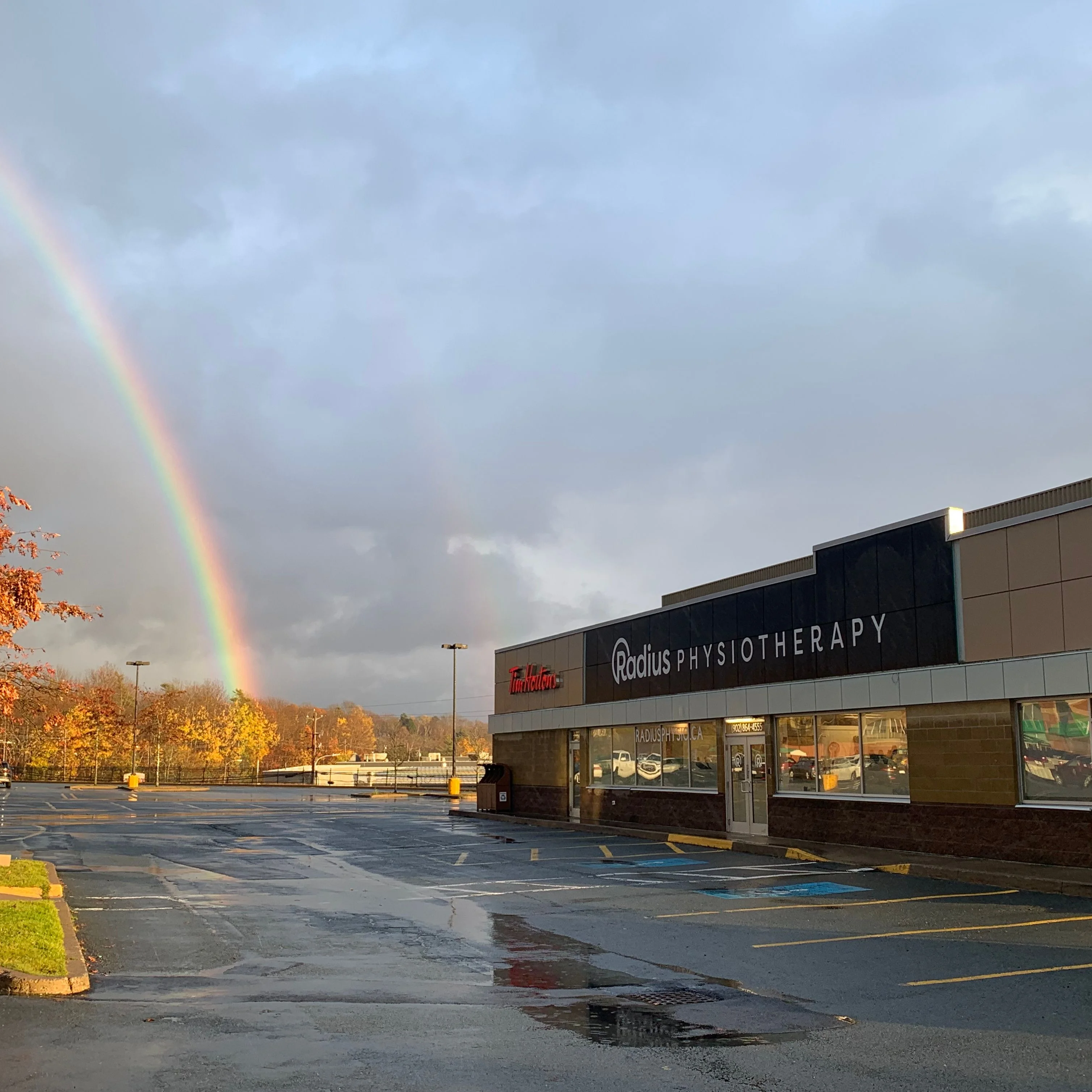 The Radius Physiotherapy storefront on First Lake Drive, with a rainbow over the parking lot after rain.
