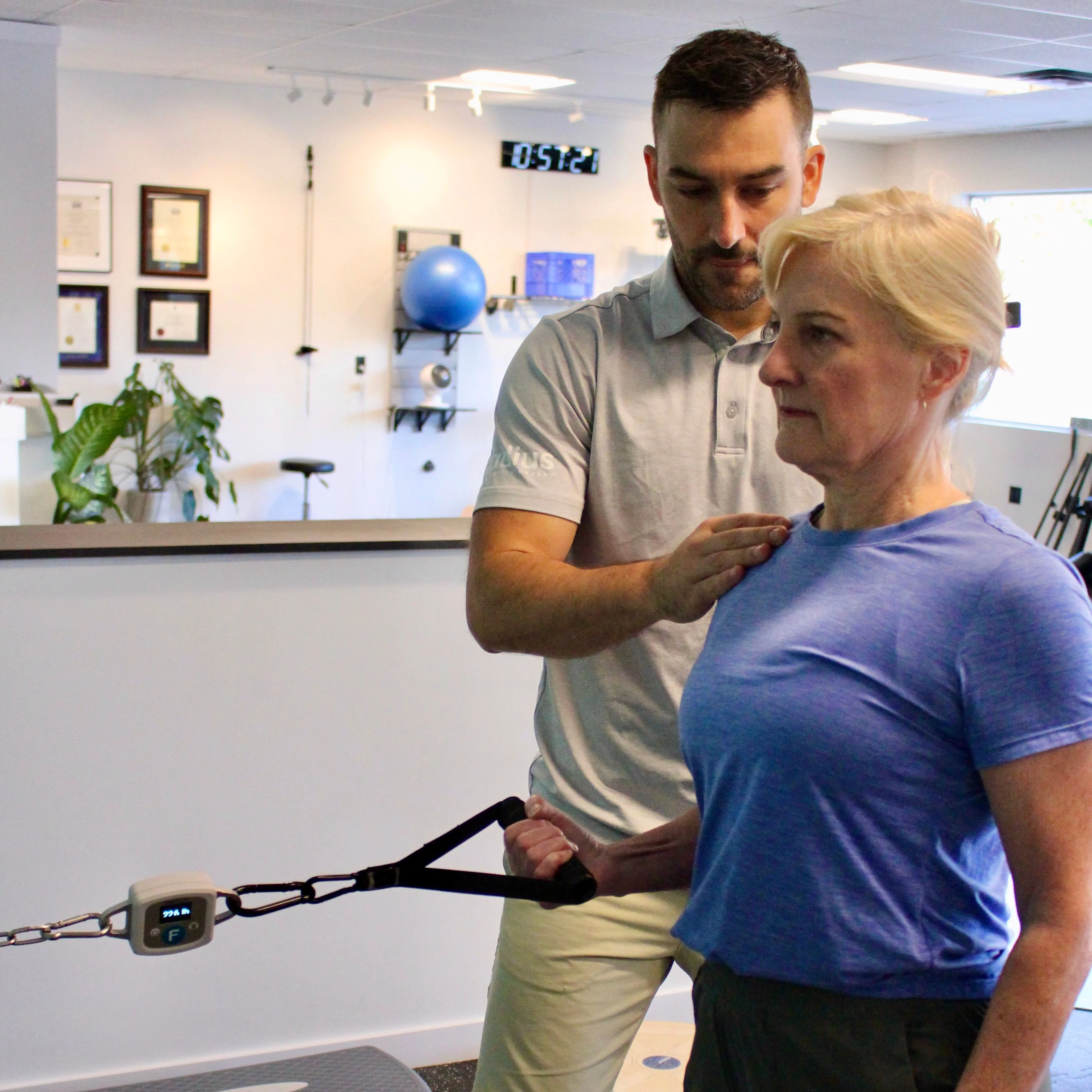 A Radius physiotherapist guiding a patient's shoulder during a cable resistance exercise.