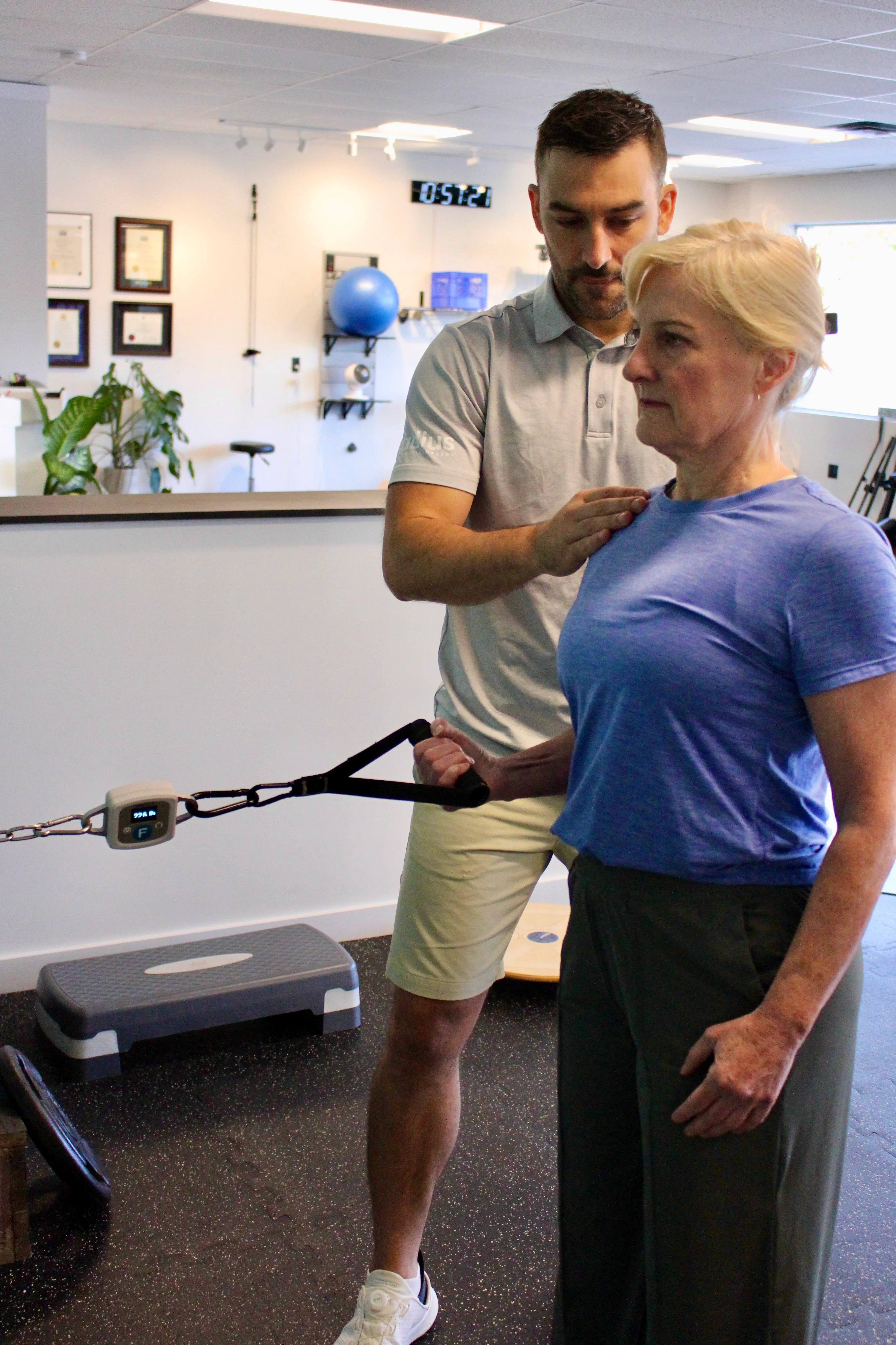 A Radius physiotherapist guiding a patient's shoulder during a cable resistance exercise.