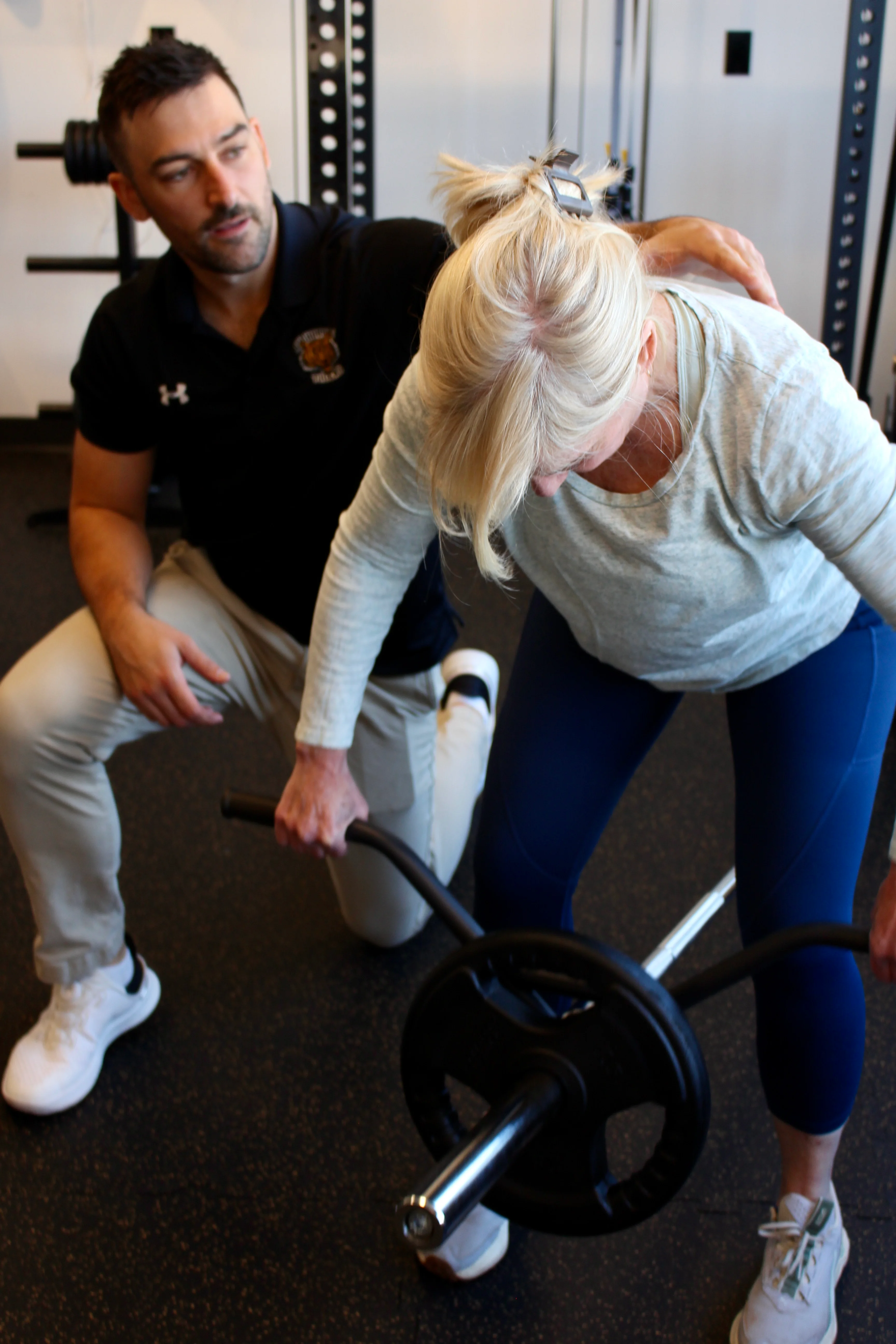A Radius physiotherapist kneeling beside a patient and guiding her shoulder through a weighted row.