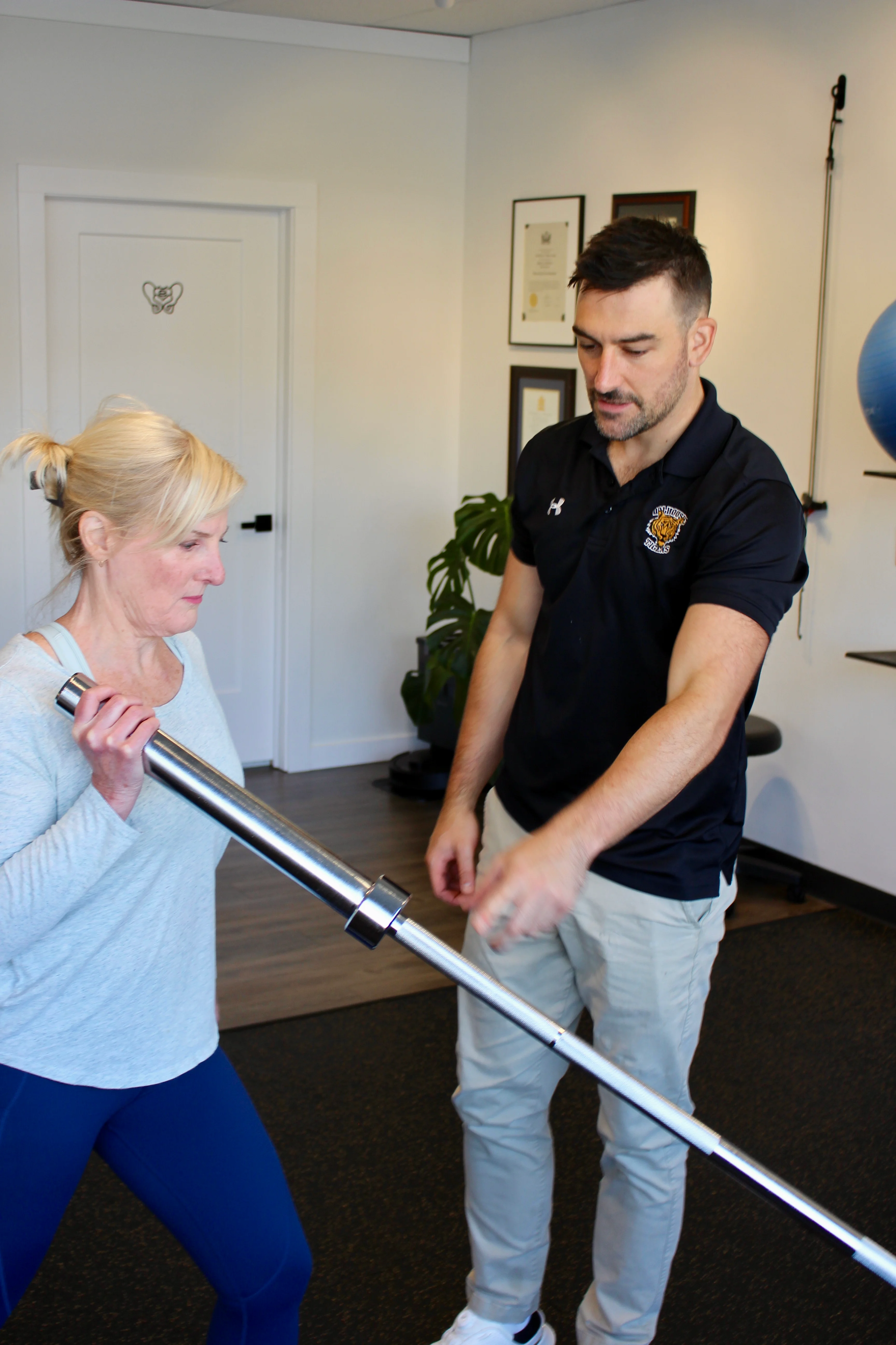 A Radius physiotherapist coaching a patient through a lunge holding a barbell across her shoulder.